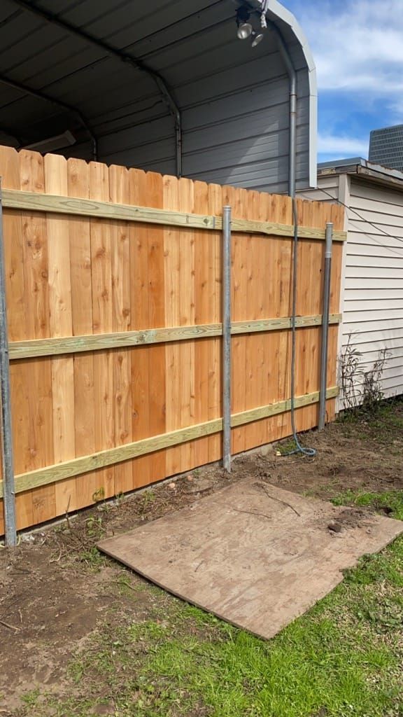 A wooden fence is sitting next to a shed in a backyard.