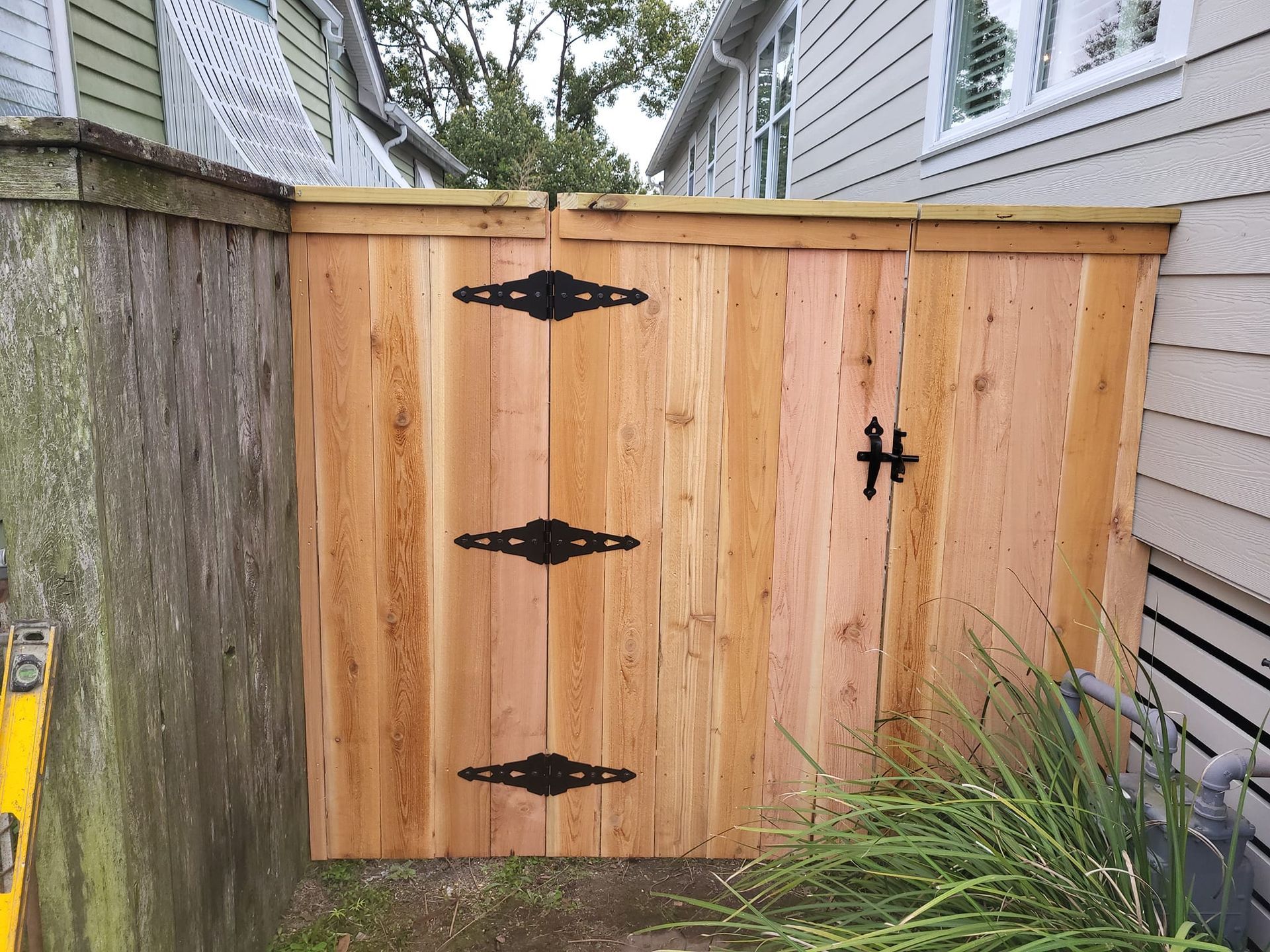 A wooden fence with black hinges is next to a house.