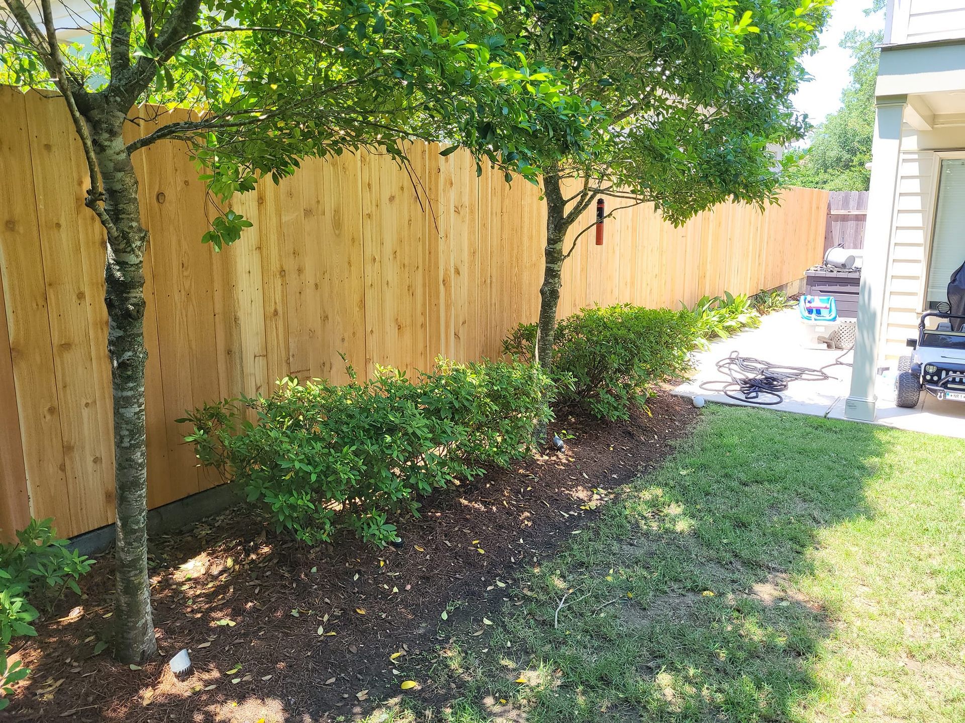 A wooden fence is surrounded by trees and bushes in a backyard.