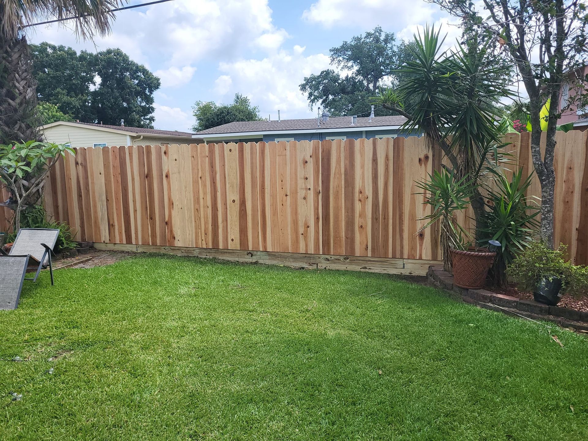 A wooden fence surrounds a lush green lawn in a backyard.