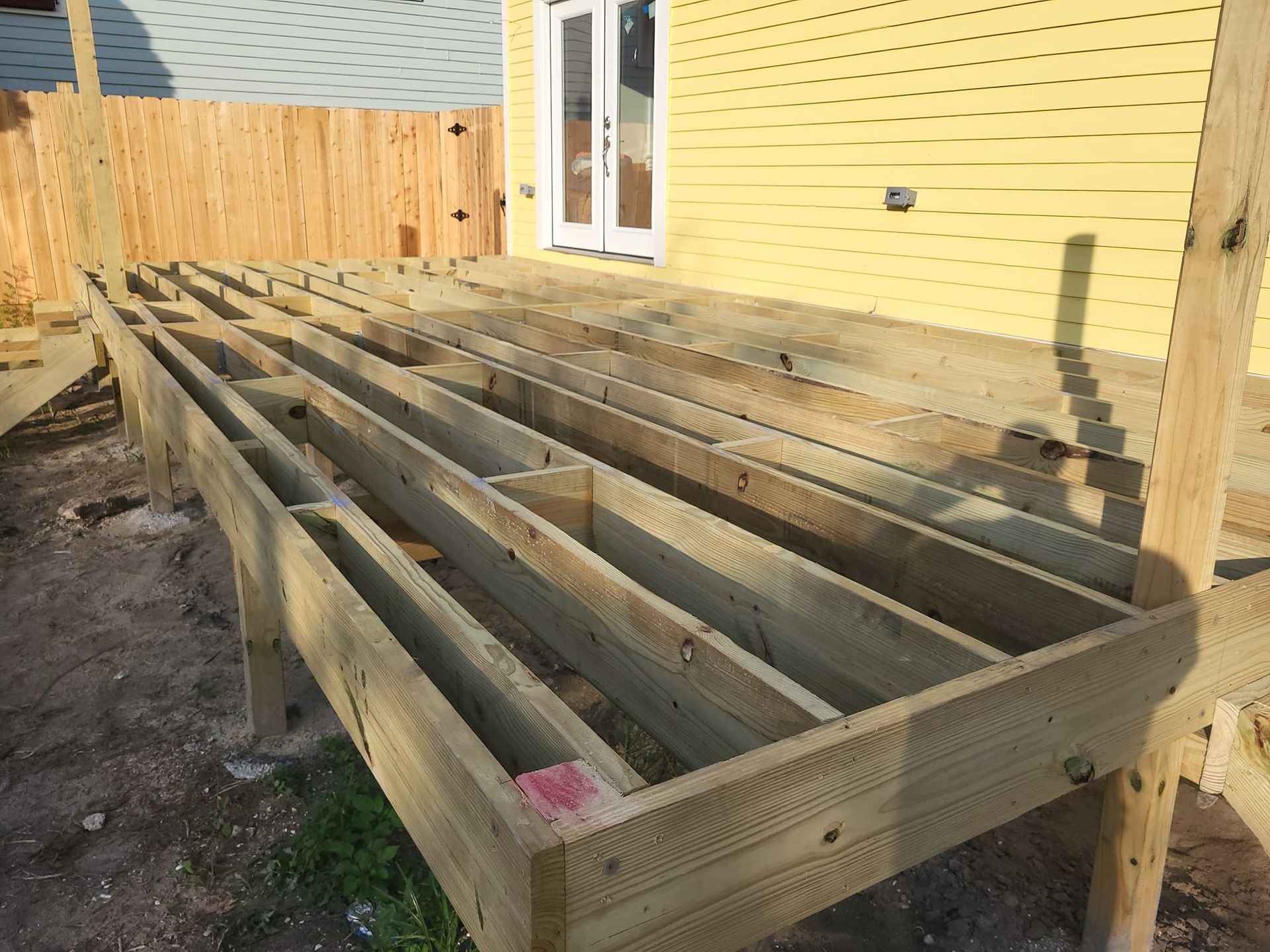 A wooden deck is being built in front of a yellow house.