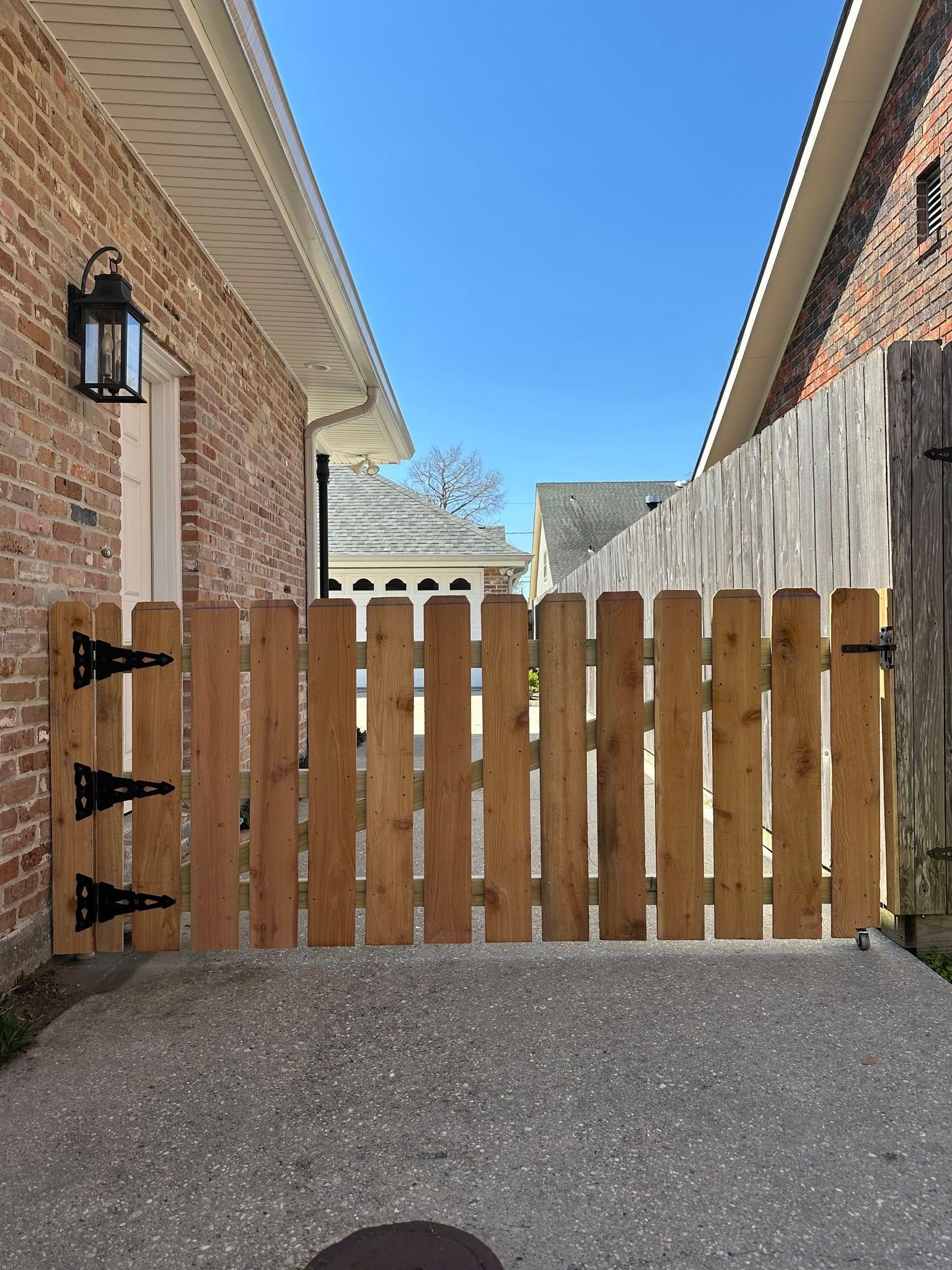 A wooden fence is sitting in the middle of a driveway next to a brick building.