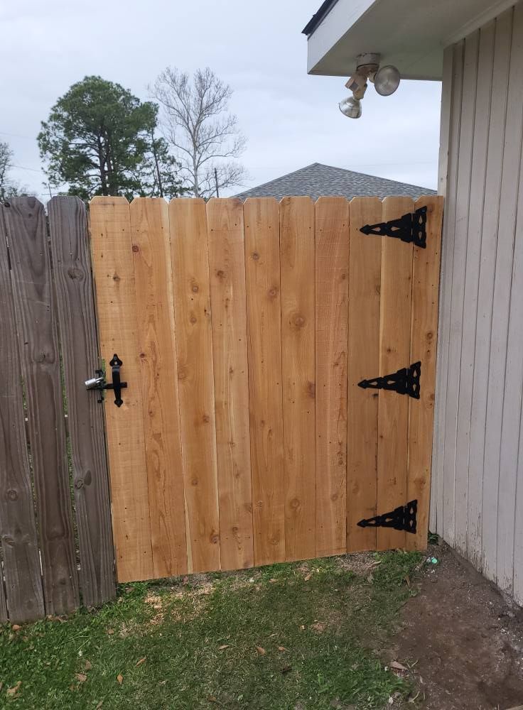 A wooden gate with black hinges is sitting next to a house.