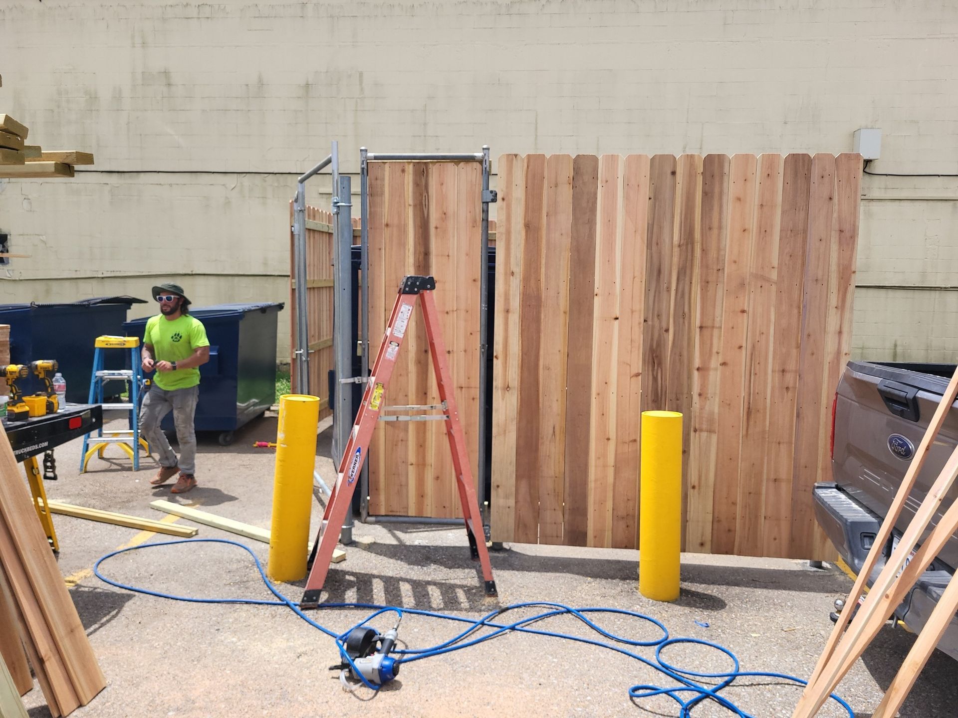 A man is working on a wooden fence in a parking lot.