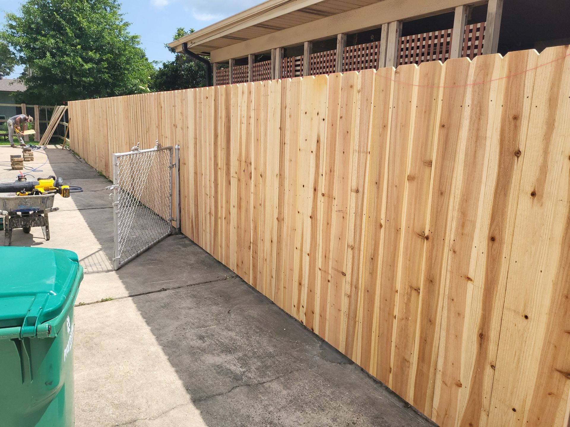 Newly built wooden fence along a concrete path with a green trash bin.