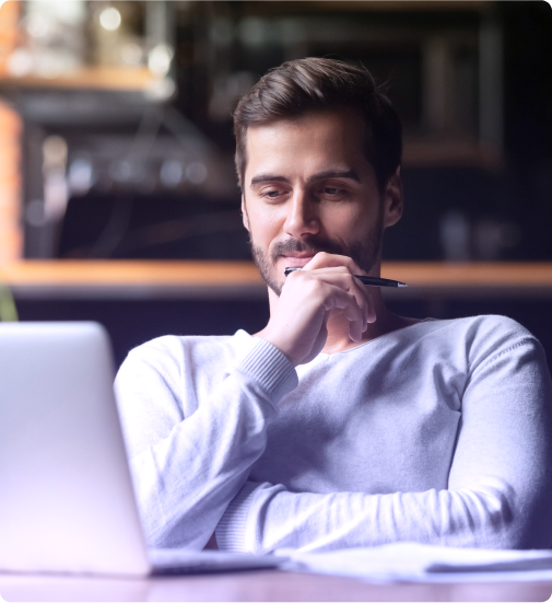 um homem está sentado a uma mesa com um laptop e uma caneta na mão