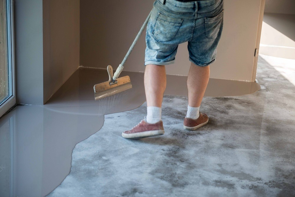 a man is painting a concrete floor with a broom .