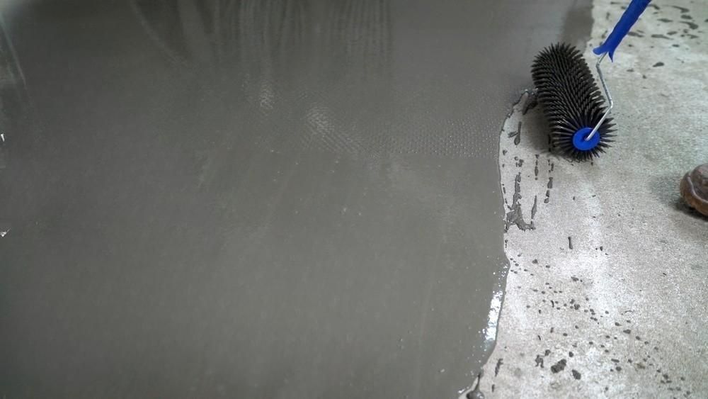 two men are painting a concrete floor with a roller .