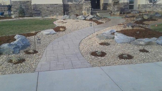 A brick walkway leading to a house surrounded by rocks and gravel.