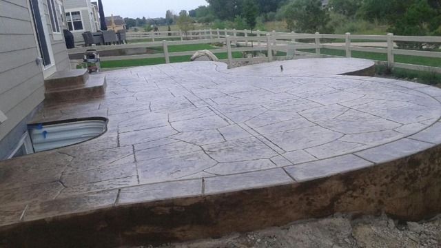 A concrete patio with a fence in the background and a house in the background.