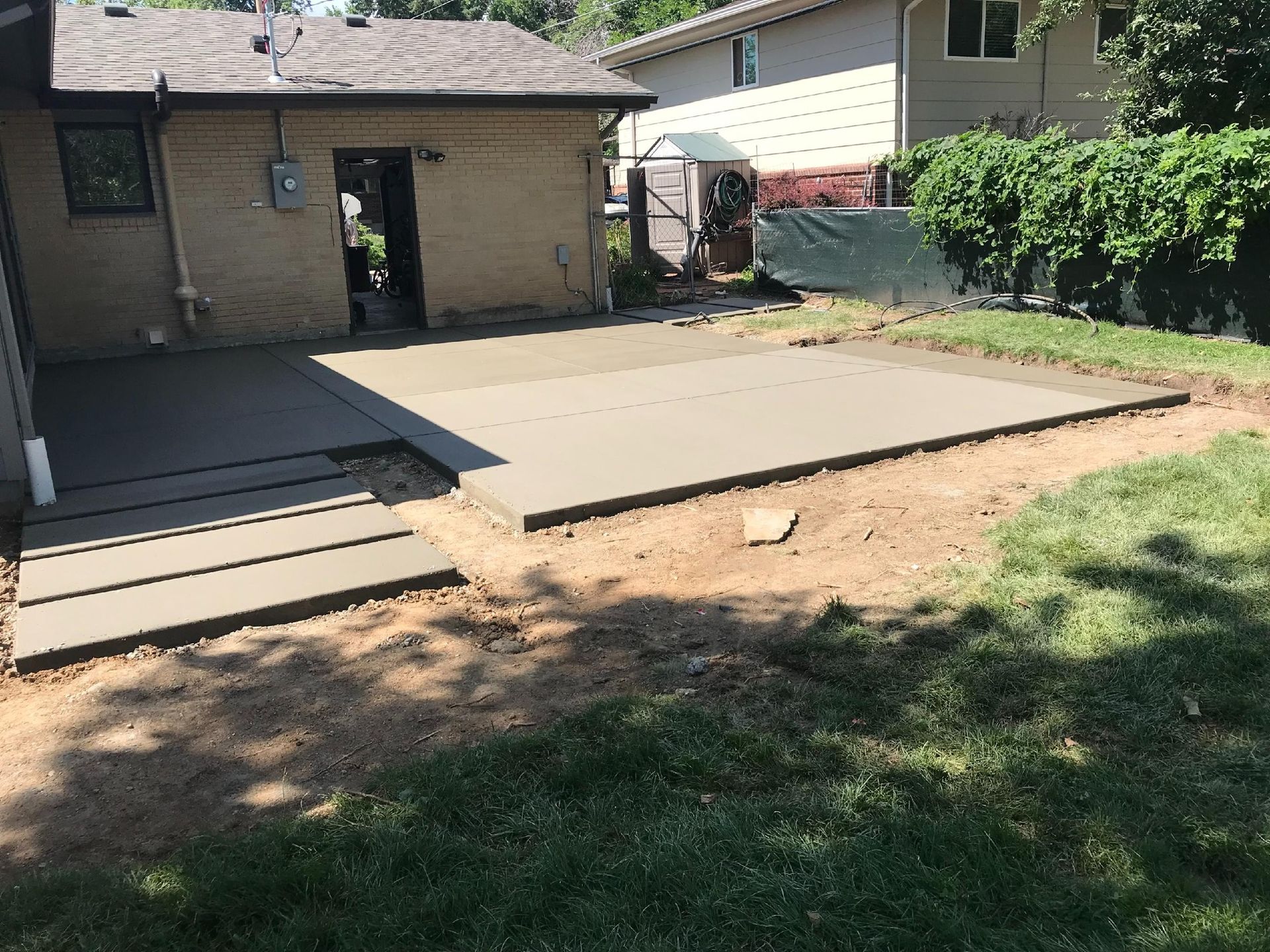 A concrete patio is being built in the backyard of a house.