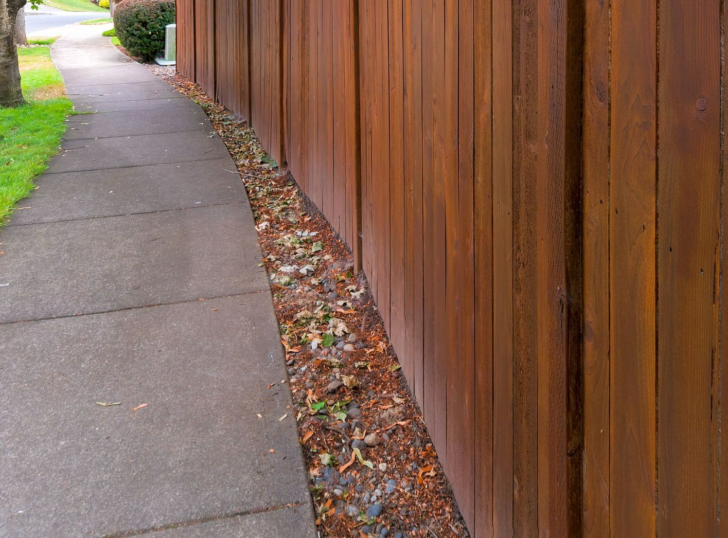 A wooden fence along a sidewalk with trees in the background.