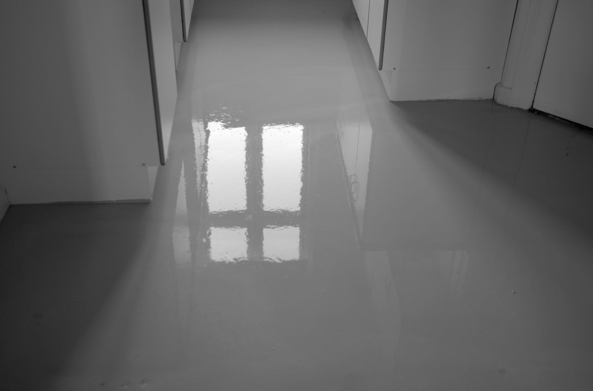 A black and white photo of a hallway with a reflection of a window in the floor.