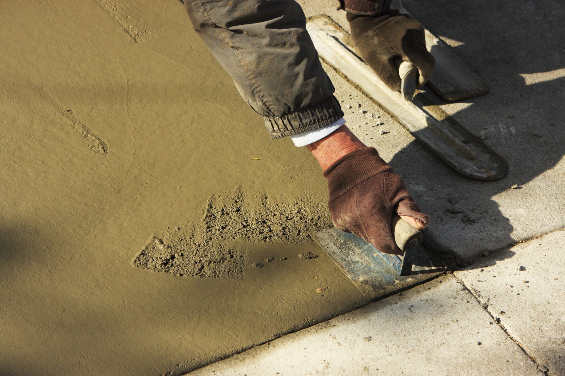 A person is using a trowel to spread concrete on a sidewalk.