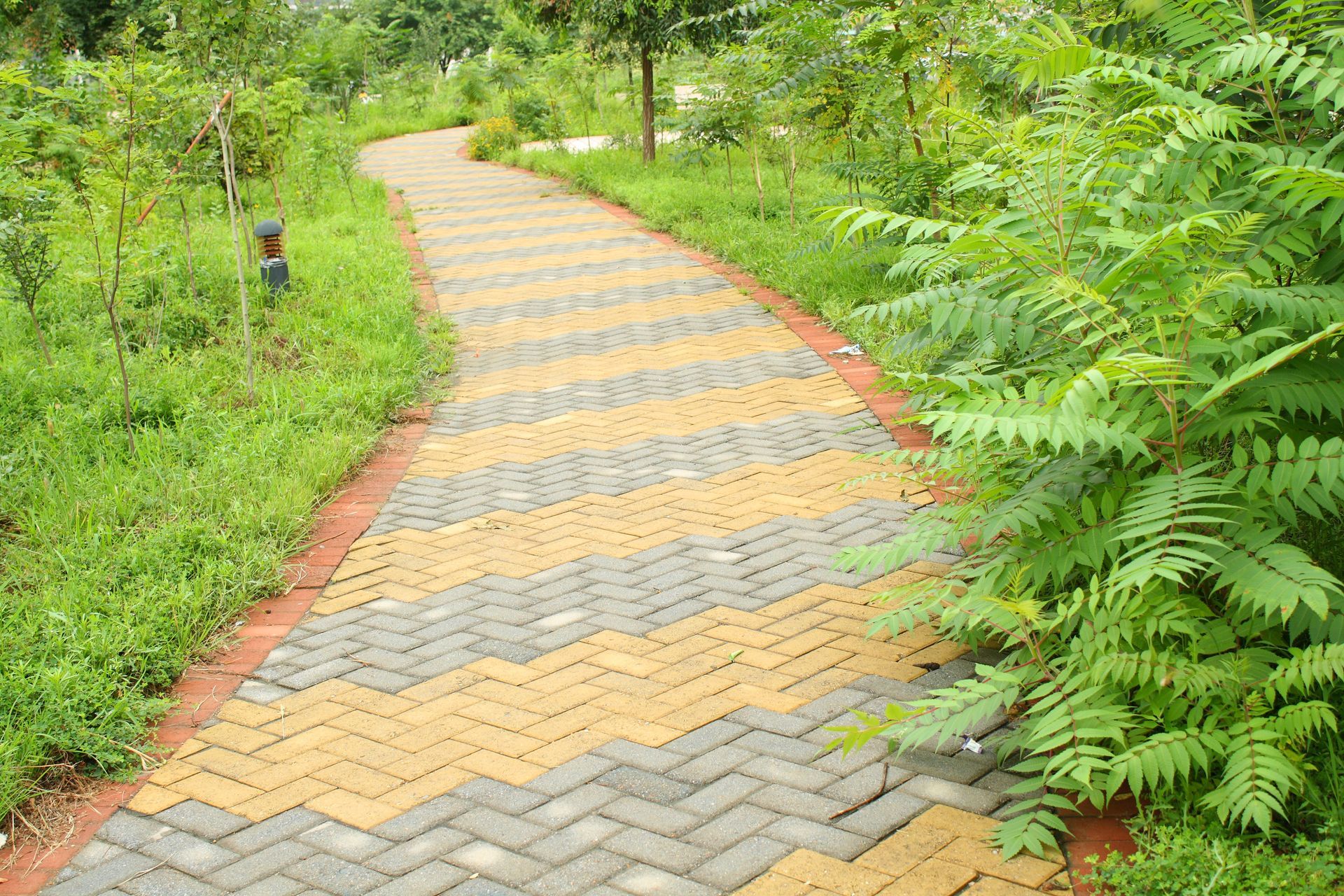A brick walkway in a park surrounded by grass and trees.