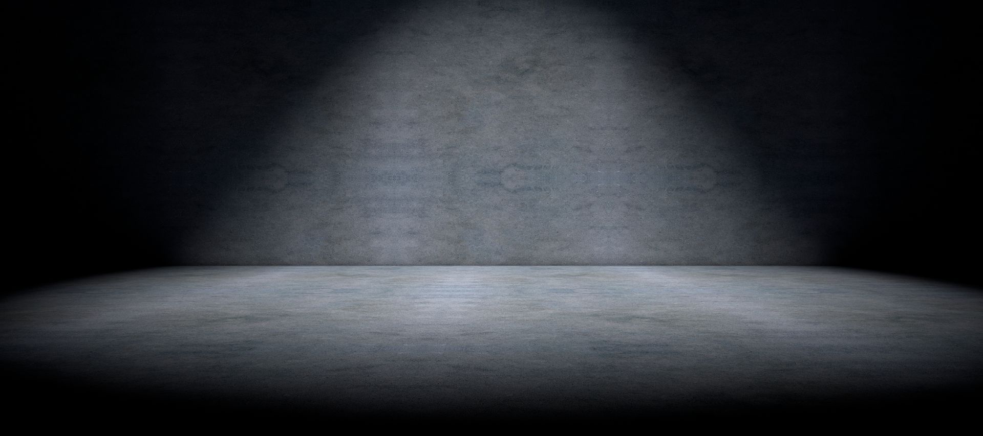 A spotlight is shining on a concrete floor in a dark room.