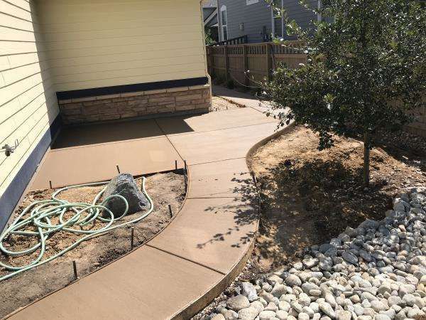A concrete walkway is being built in the backyard of a house.