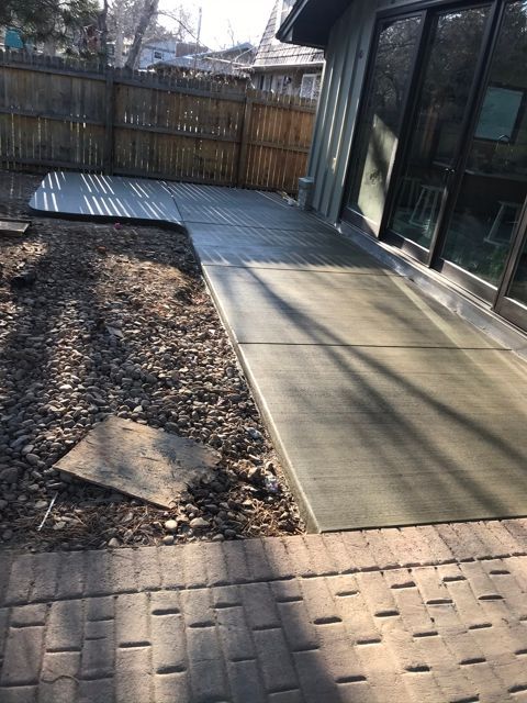 A patio with a brick walkway and a fence in the backyard of a house.