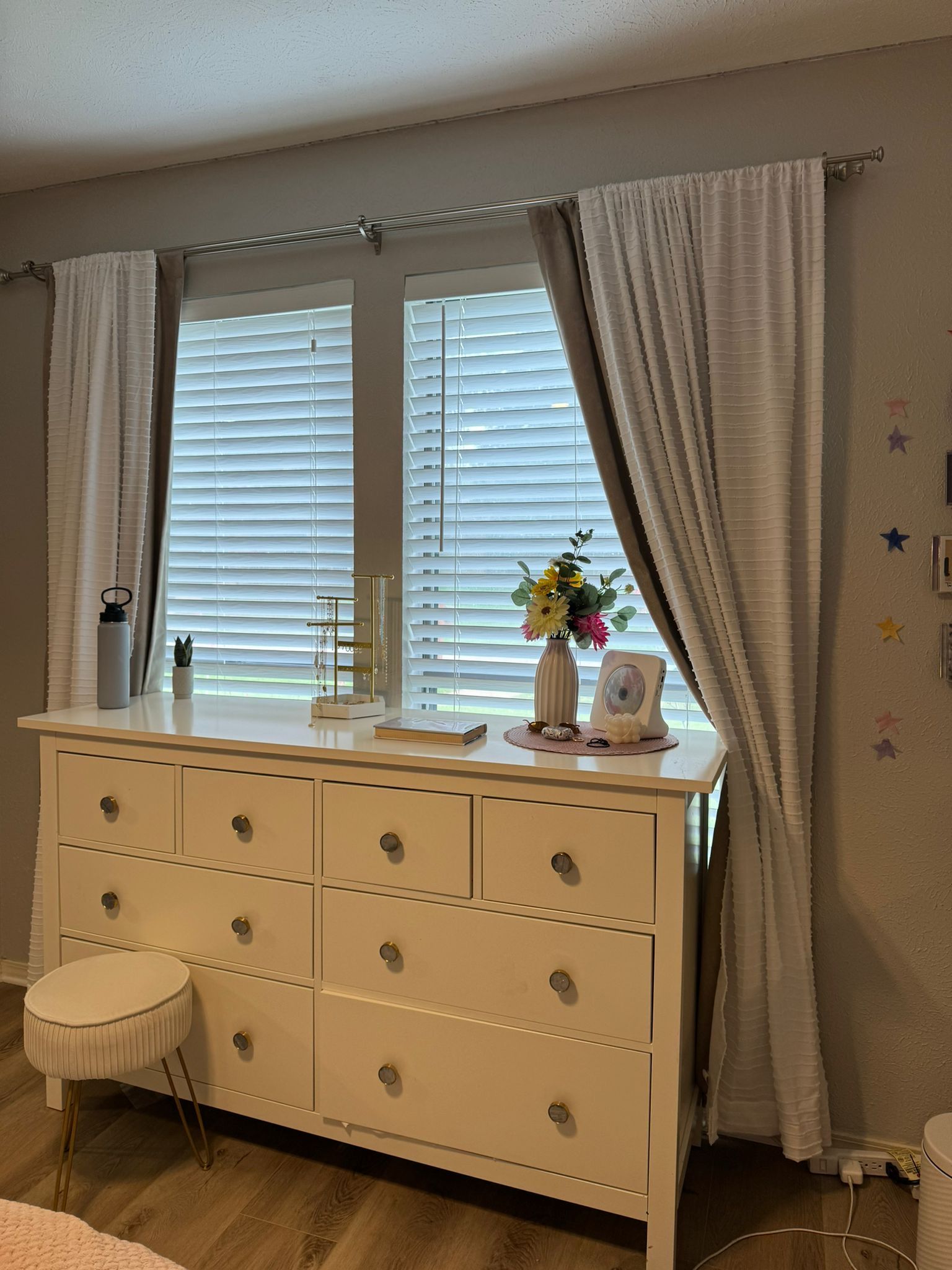 A bedroom with a dresser and a window with blinds.