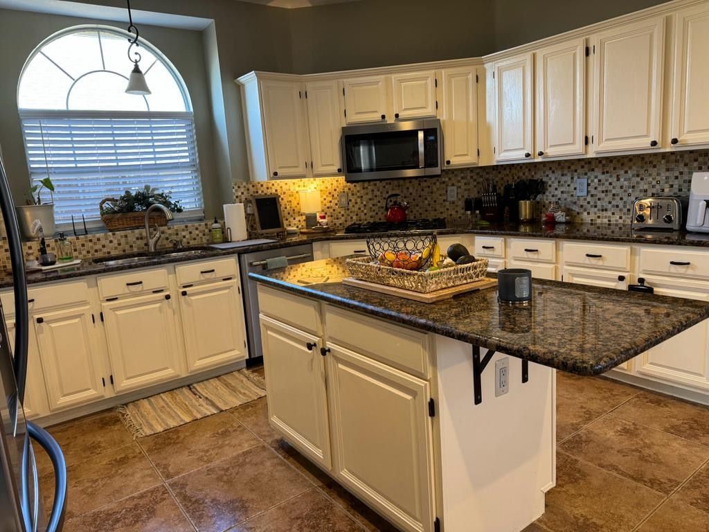 A kitchen with white cabinets , granite counter tops , stainless steel appliances and a large island.