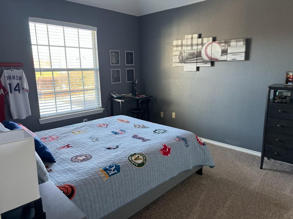 A bedroom with a bed , dresser , desk and window.
