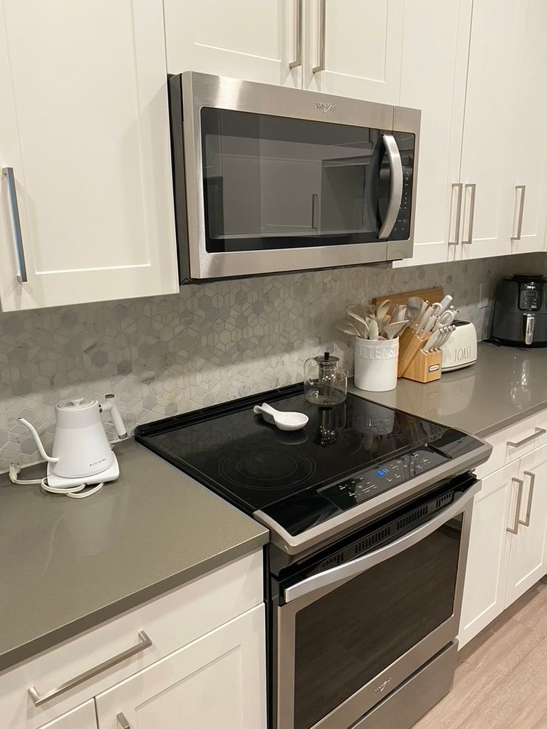A kitchen with a stove , oven , microwave and white cabinets.