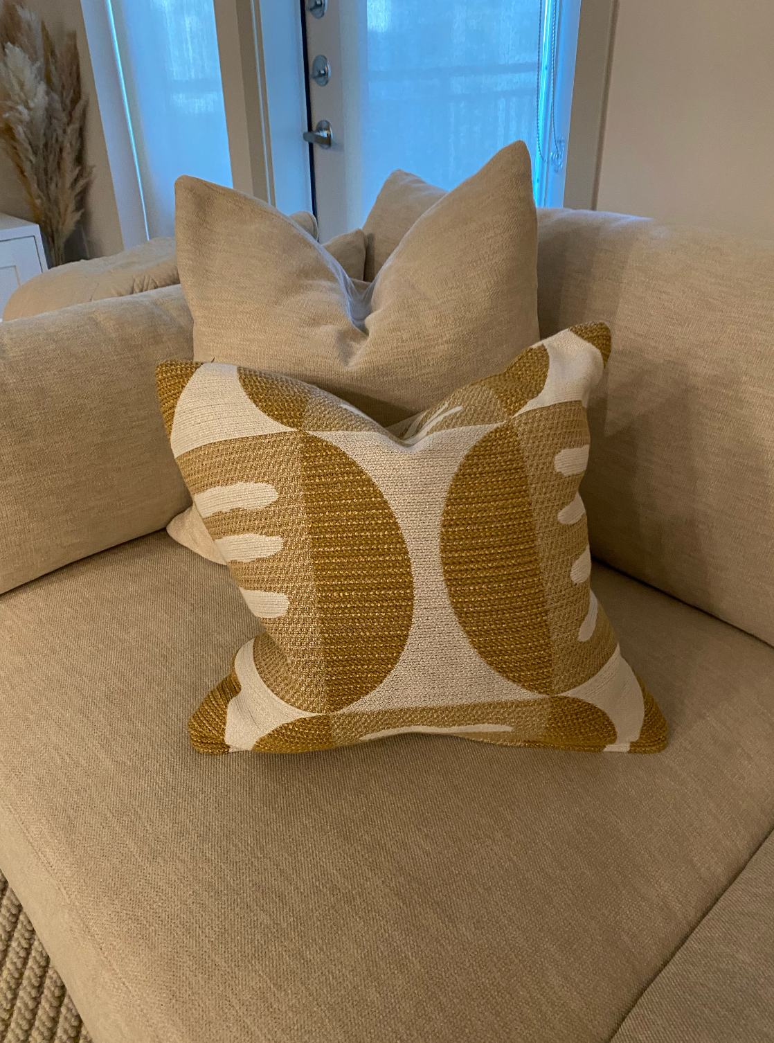 A yellow and white pillow is sitting on a beige couch.