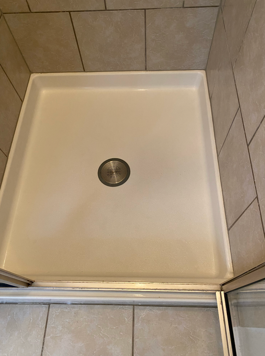 A white shower stall with a drain in a bathroom.
