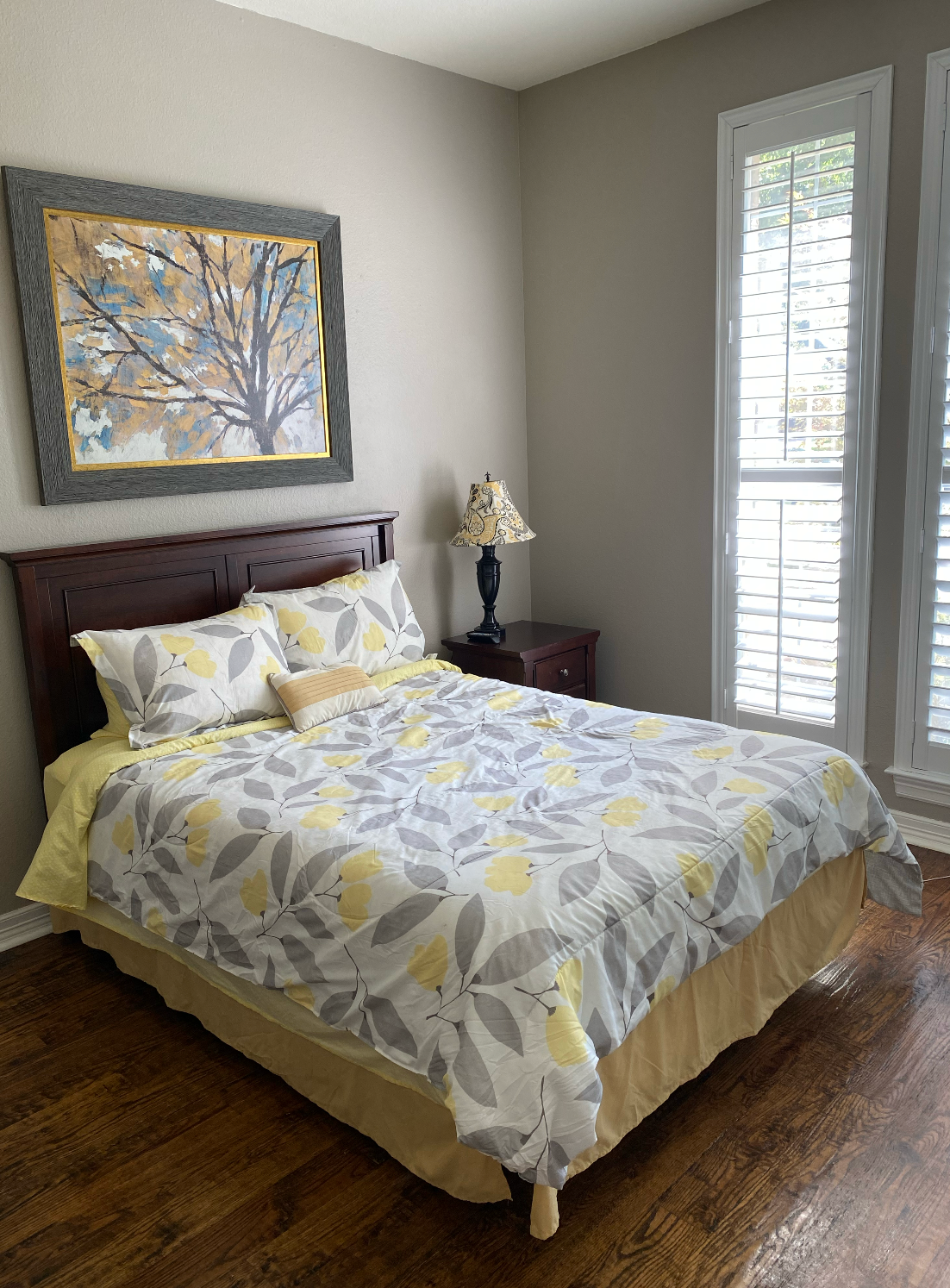 A bedroom with a bed , nightstand , lamp and shutters.