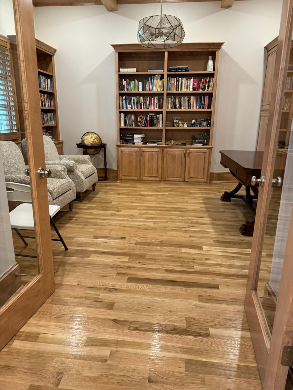 A living room with hardwood floors , bookshelves , chairs and a desk.