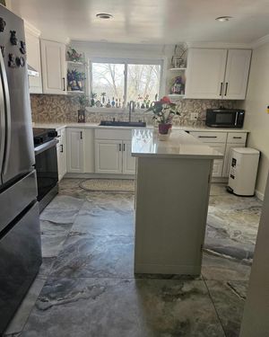 A kitchen with white cabinets, a central island, grey stone flooring, and a stainless steel refrigerator.