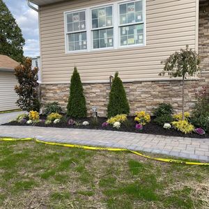 A modern house exterior with tan siding and stone veneer, fronted by a stone walkway and a landscaped garden bed.