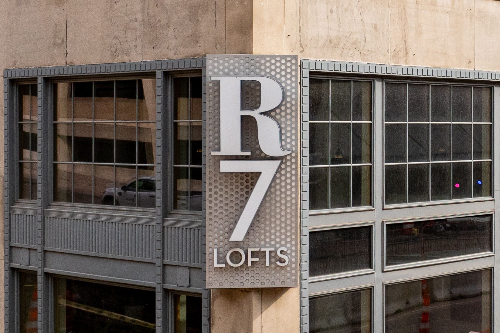 Sign for R7 Lofts on corner of building; silver letters on textured panel; windows reflect surroundings at R7 Lofts in St. Paul, MN.
