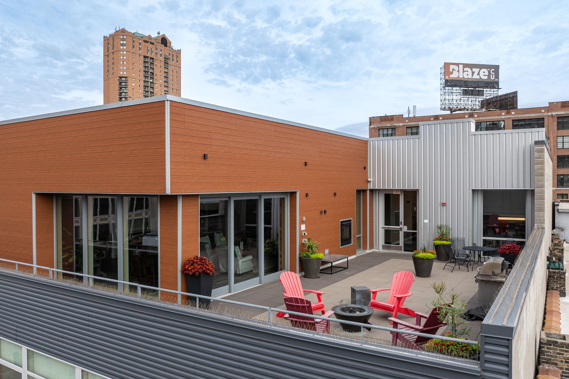 Rooftop patio with red chairs, planters, and a brick and metal building. A sign reads 