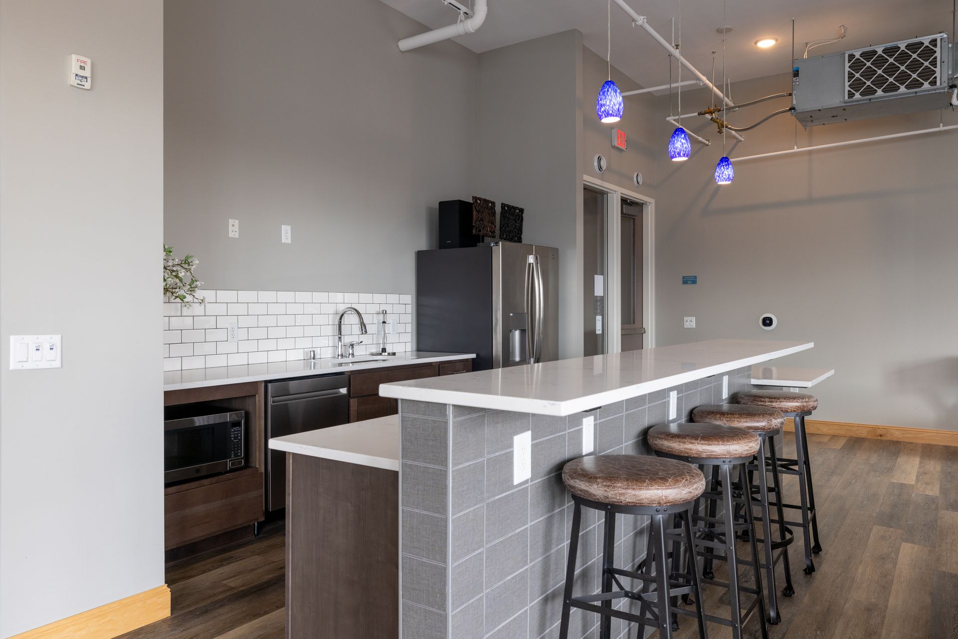 Modern kitchen with a breakfast bar and stools. Includes a fridge, microwave, sink, and pendant lights at R7 Lofts in St. Paul, MN.