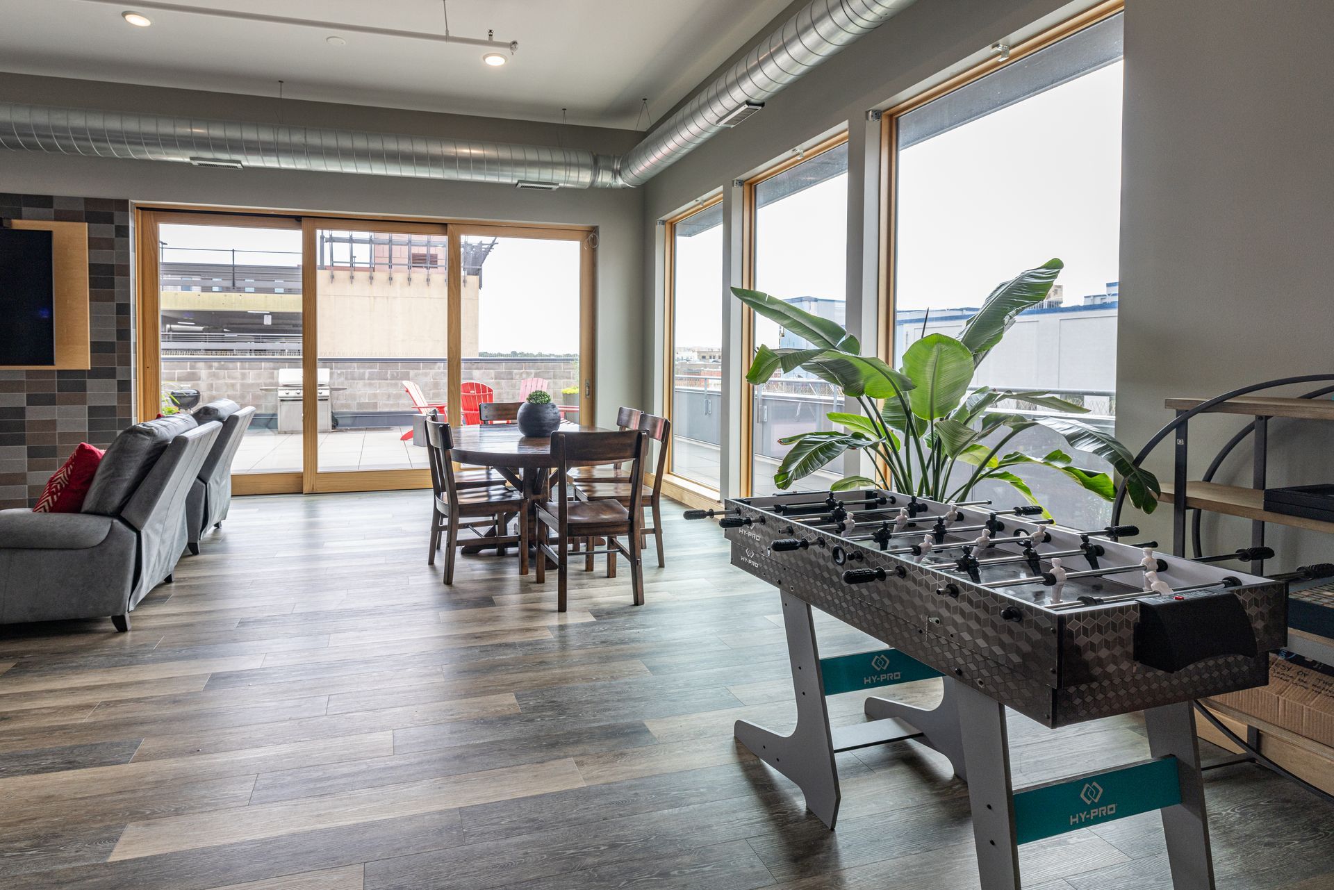 Bright, open living space with a foosball table, dining table, and large windows overlooking a city view at R7 Lofts in St. Paul, MN.