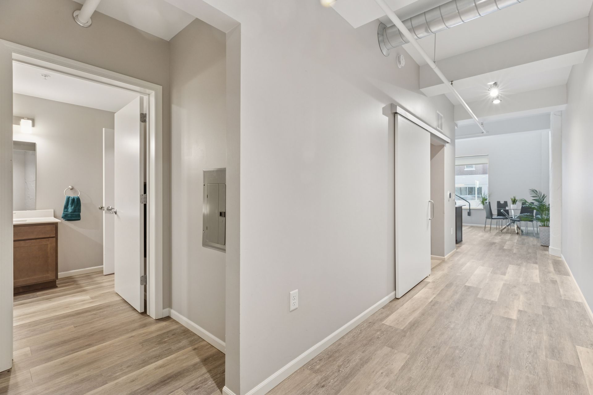 Hallway with wood floors, doors, and a bathroom on the left, leading to an open office space at R7 Lofts in St. Paul, MN.
