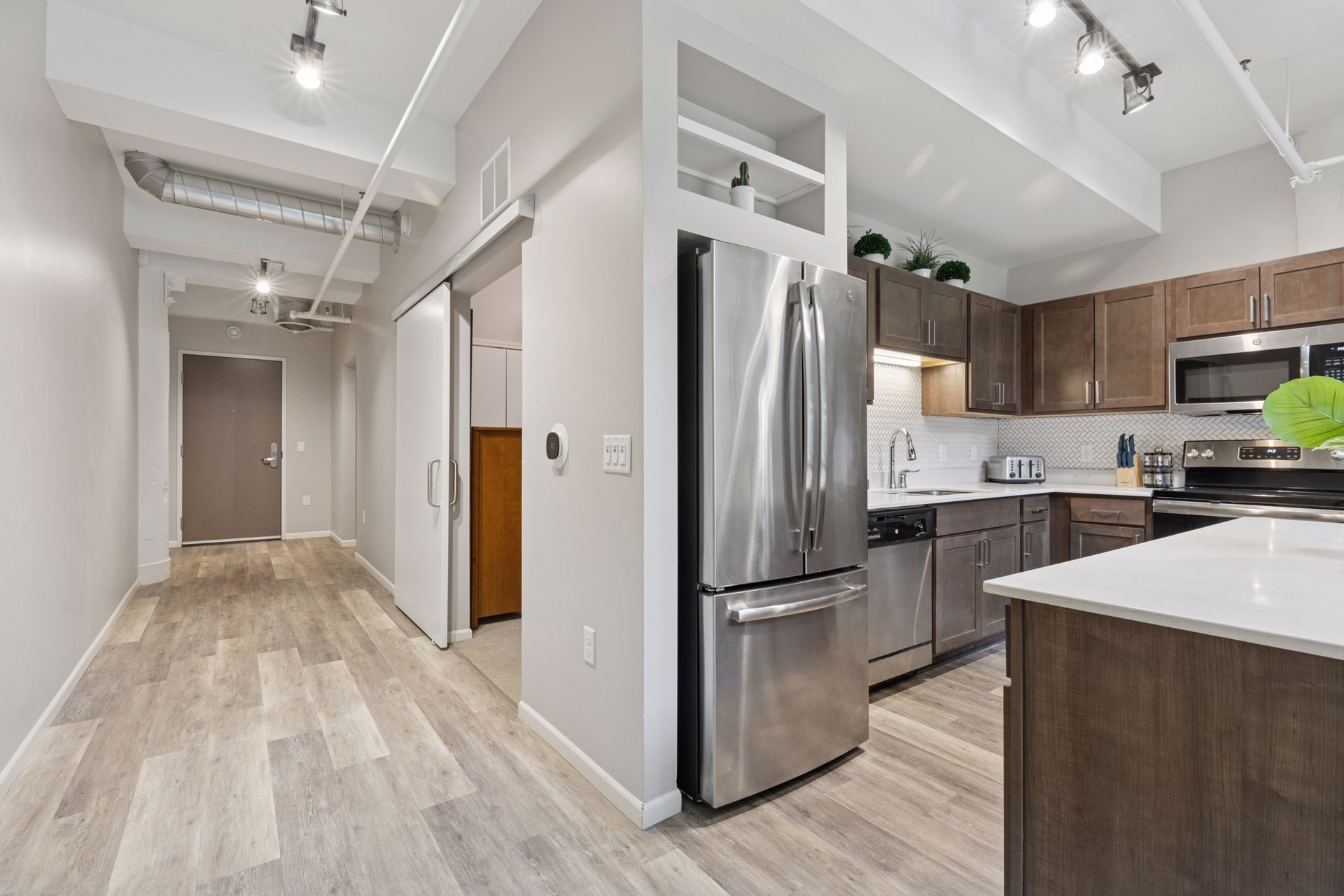 Modern kitchen and hallway with hardwood floors, stainless steel appliances, and overhead lighting at R7 Lofts in St. Paul, MN.