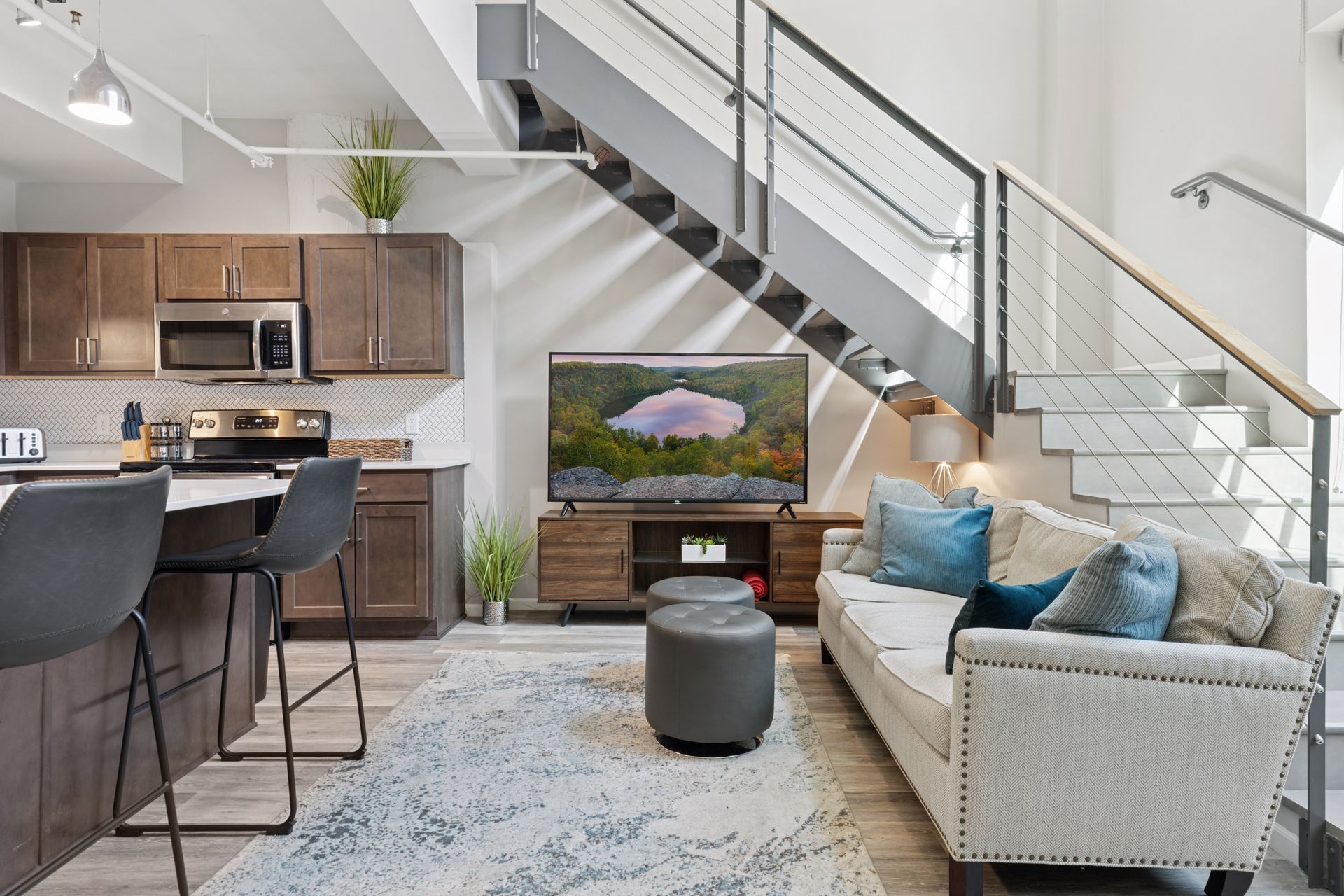 Modern loft apartment interior with kitchen, living area, and staircase. Light wood floors, dark cabinets, and a gray couch at R7 Lofts in St. Paul, MN.