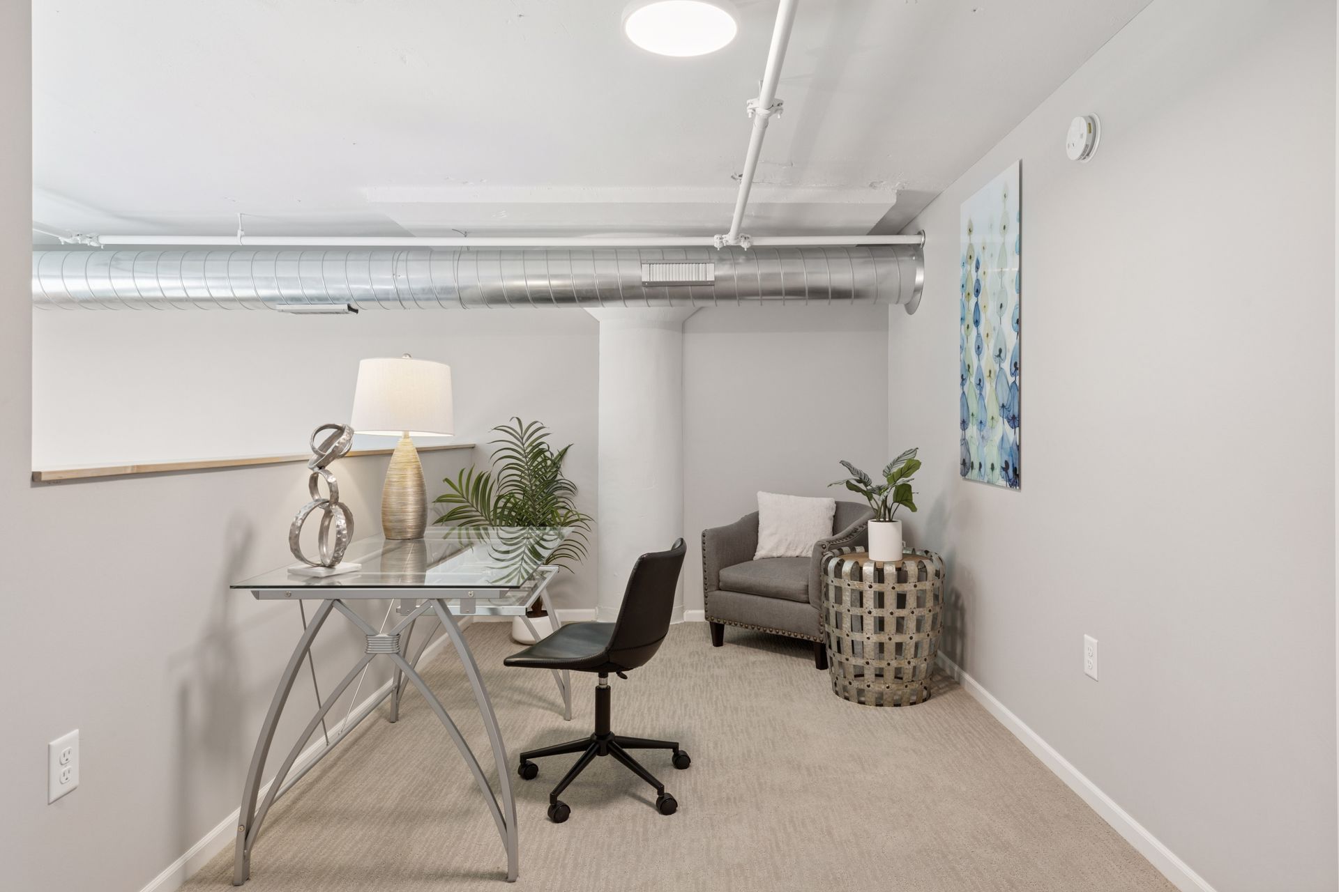 Home office with desk, chair, armchair, and art. Gray walls, beige carpet at R7 Lofts in St. Paul, MN.