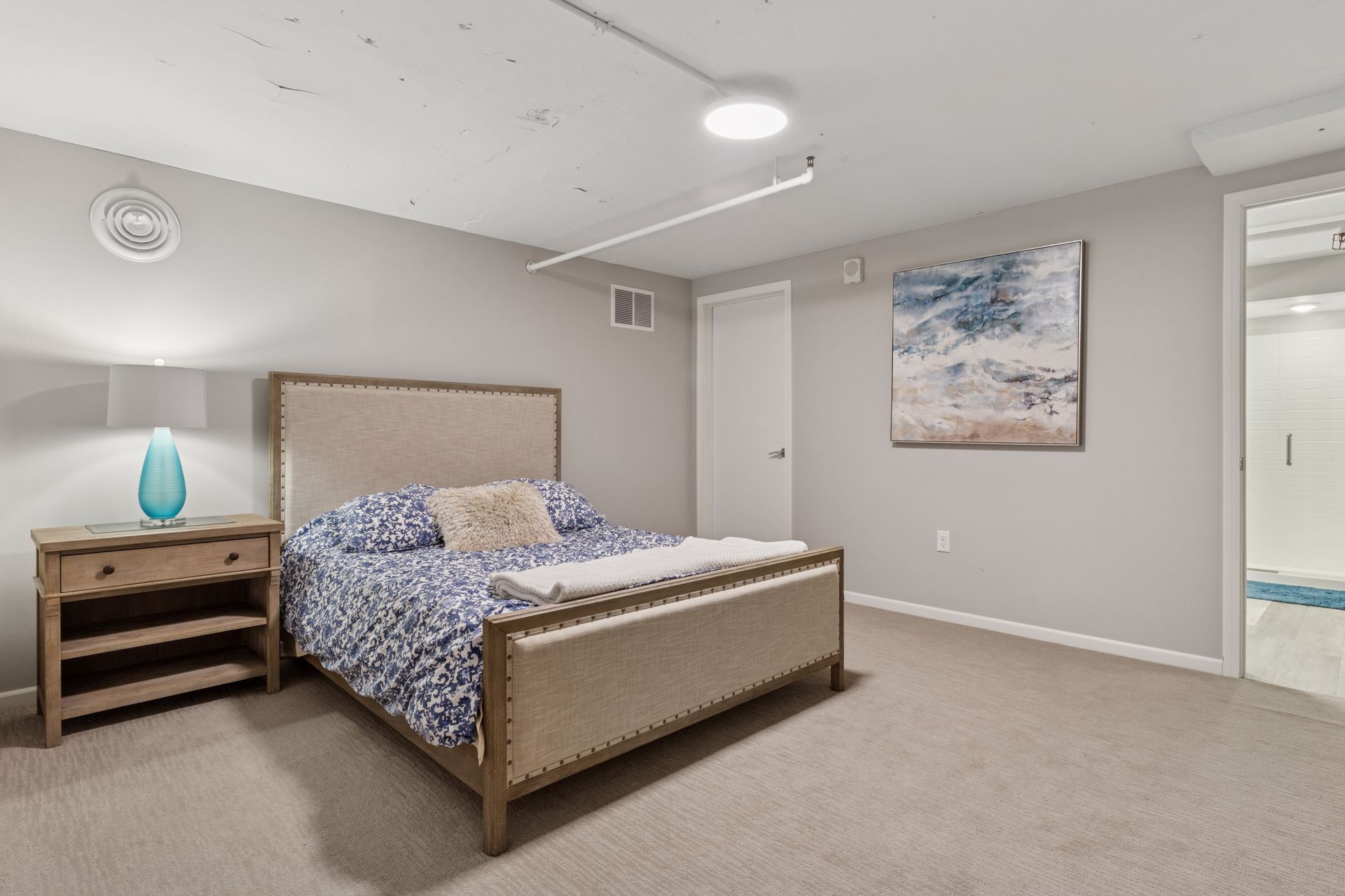 Bedroom with bed, nightstand, artwork, and doorway. Light gray walls and tan carpet.