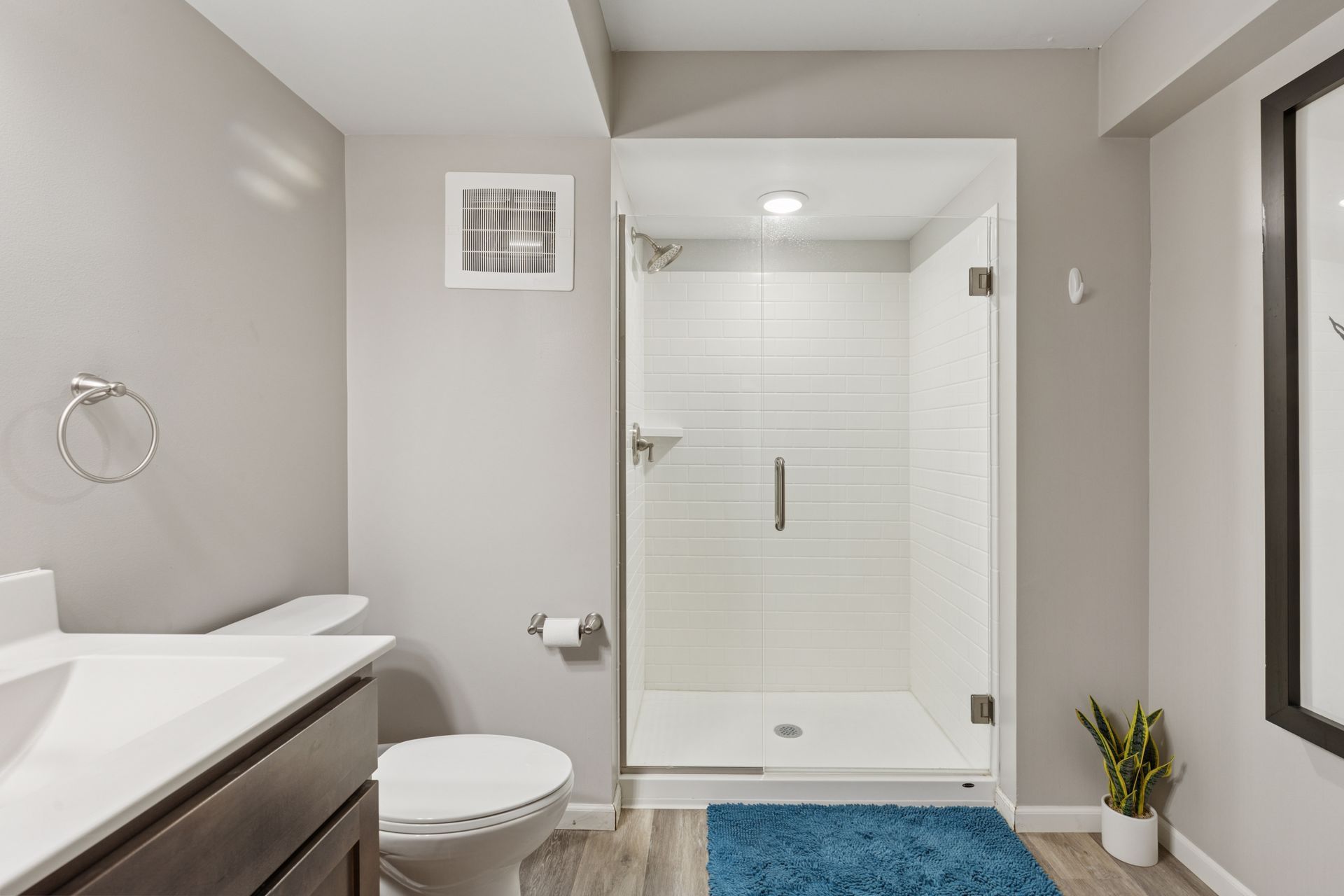 Modern bathroom with glass shower, white toilet, gray walls, and blue rug at R7 Lofts in St. Paul, MN.