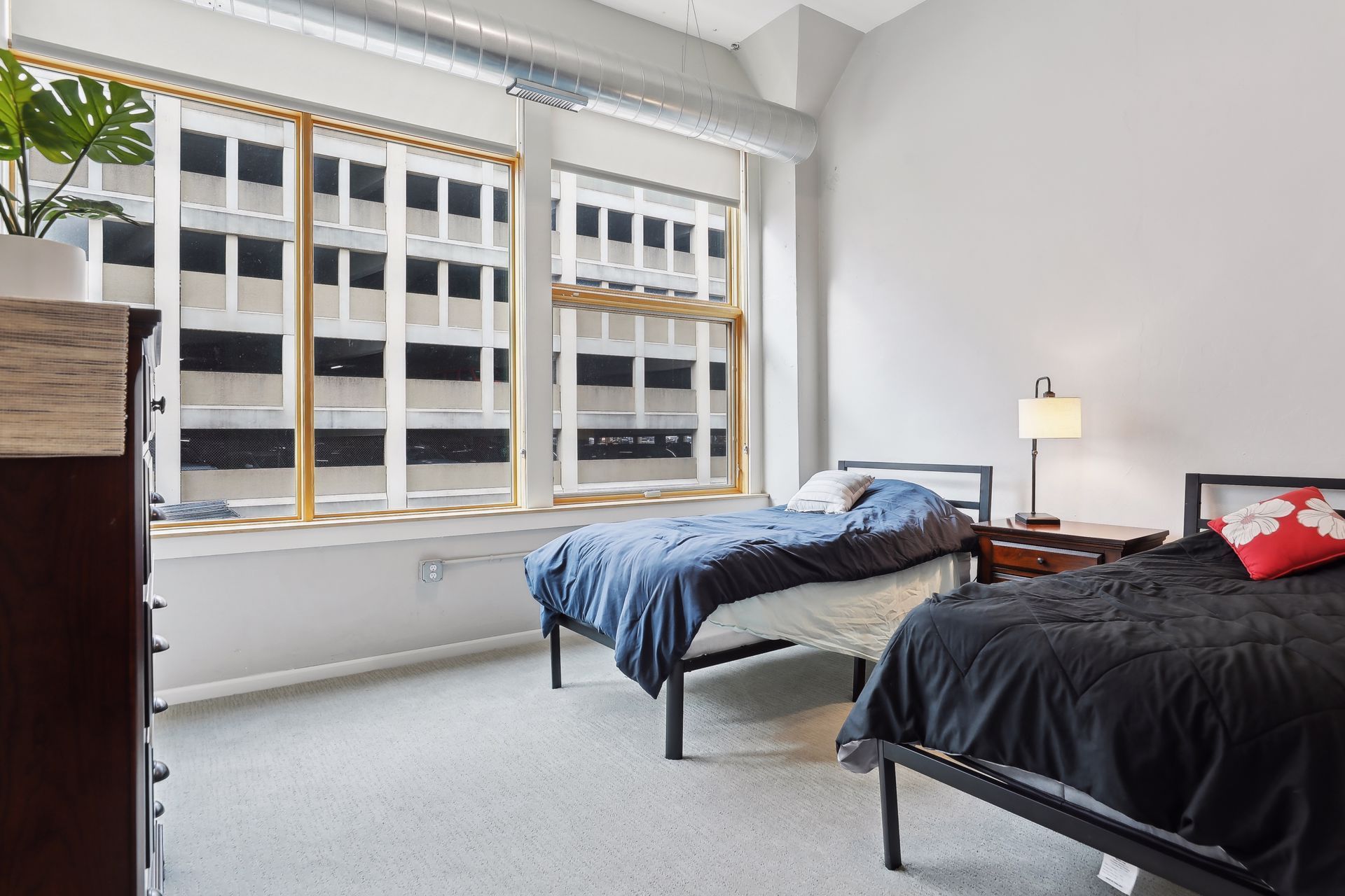 Two twin beds in a room with large windows; a dresser and lamp are also visible.