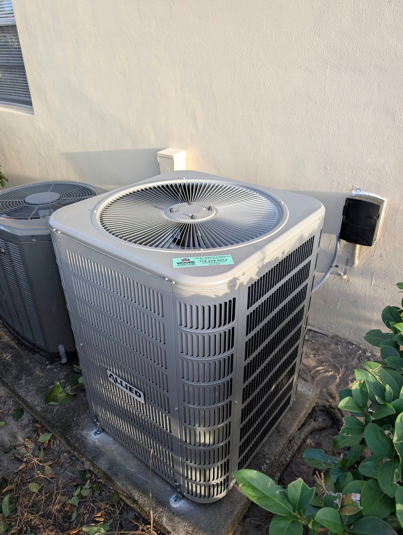 Two air conditioners are sitting next to each other on the side of a building.