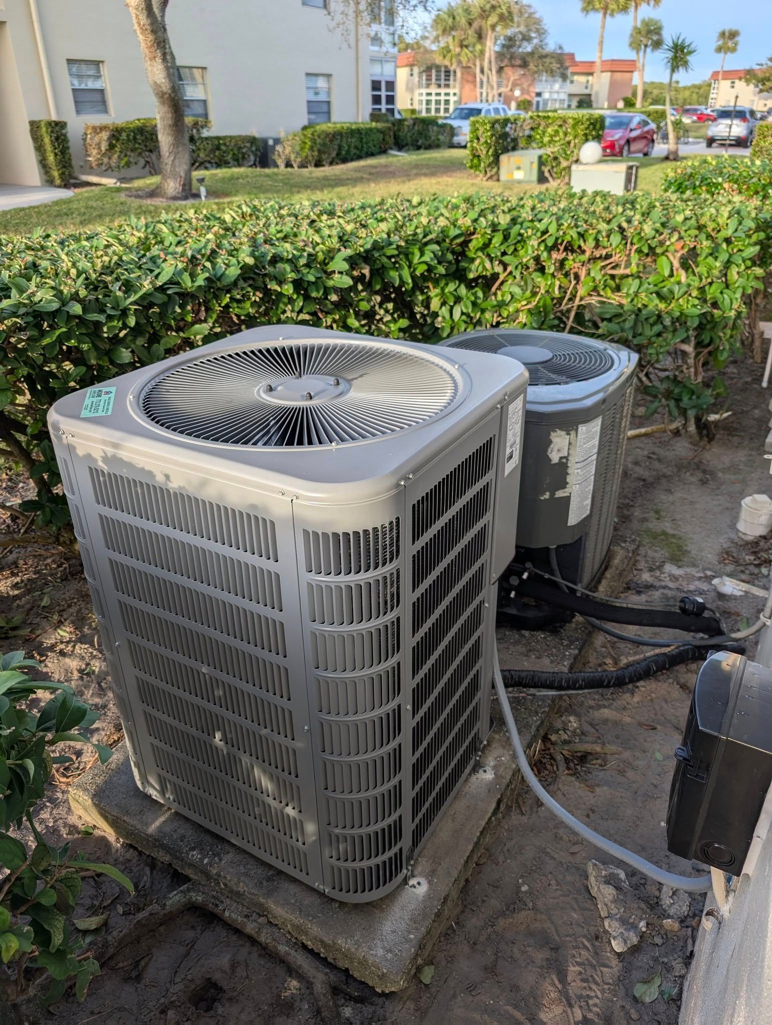 Two air conditioners are sitting next to each other in a yard.