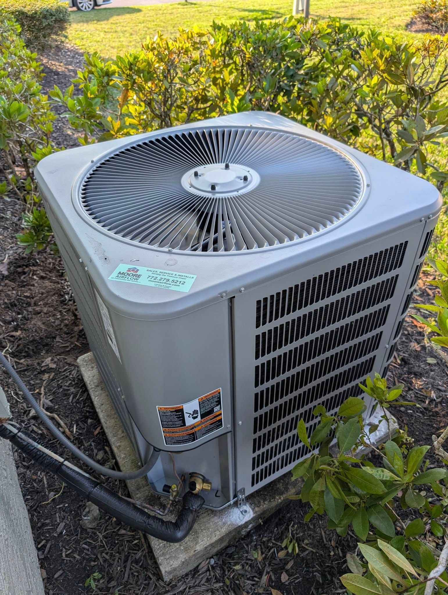 A large air conditioner is sitting on top of a concrete block next to a bush.