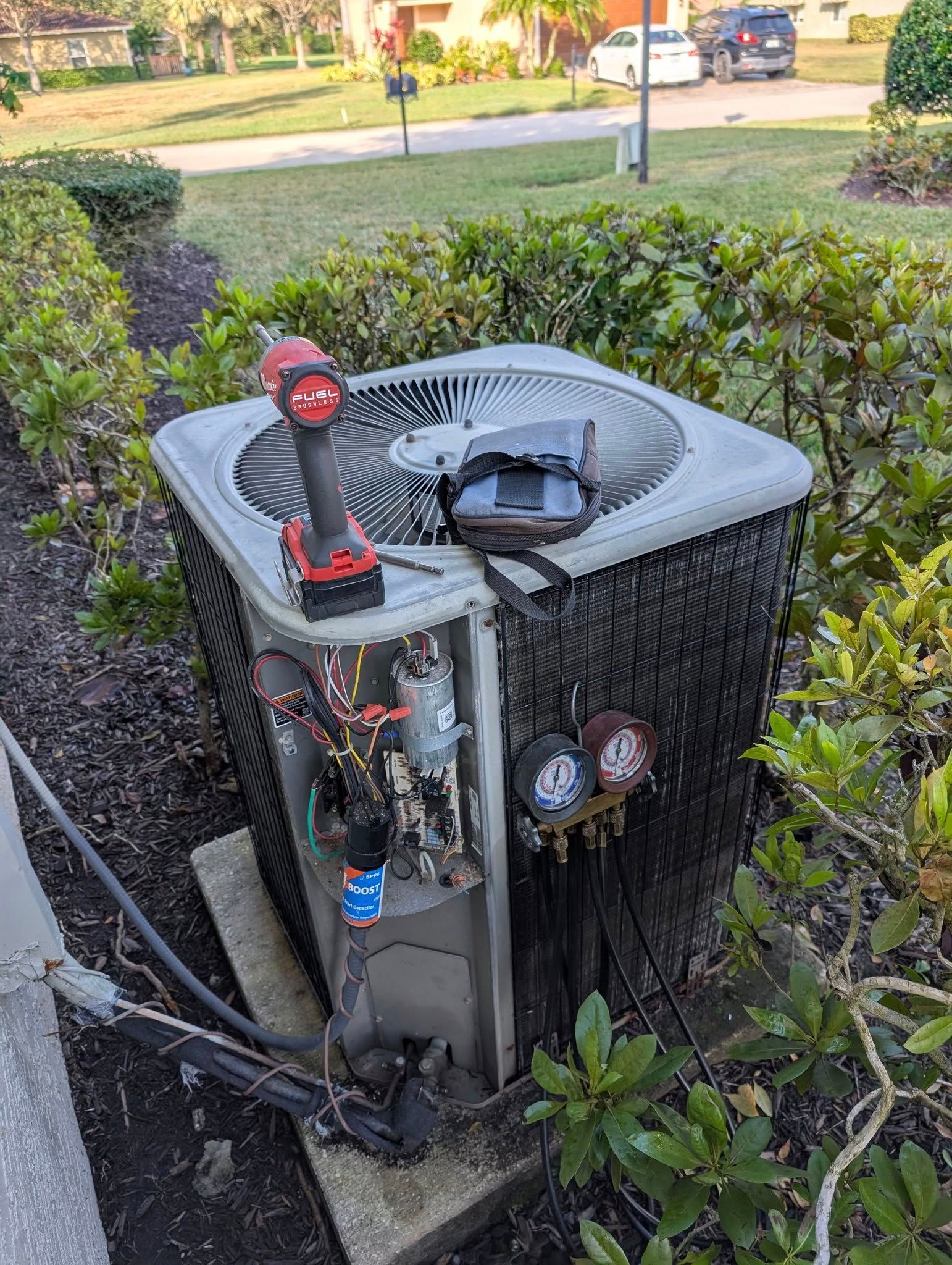 A broken air conditioner is sitting in the dirt next to a bush.