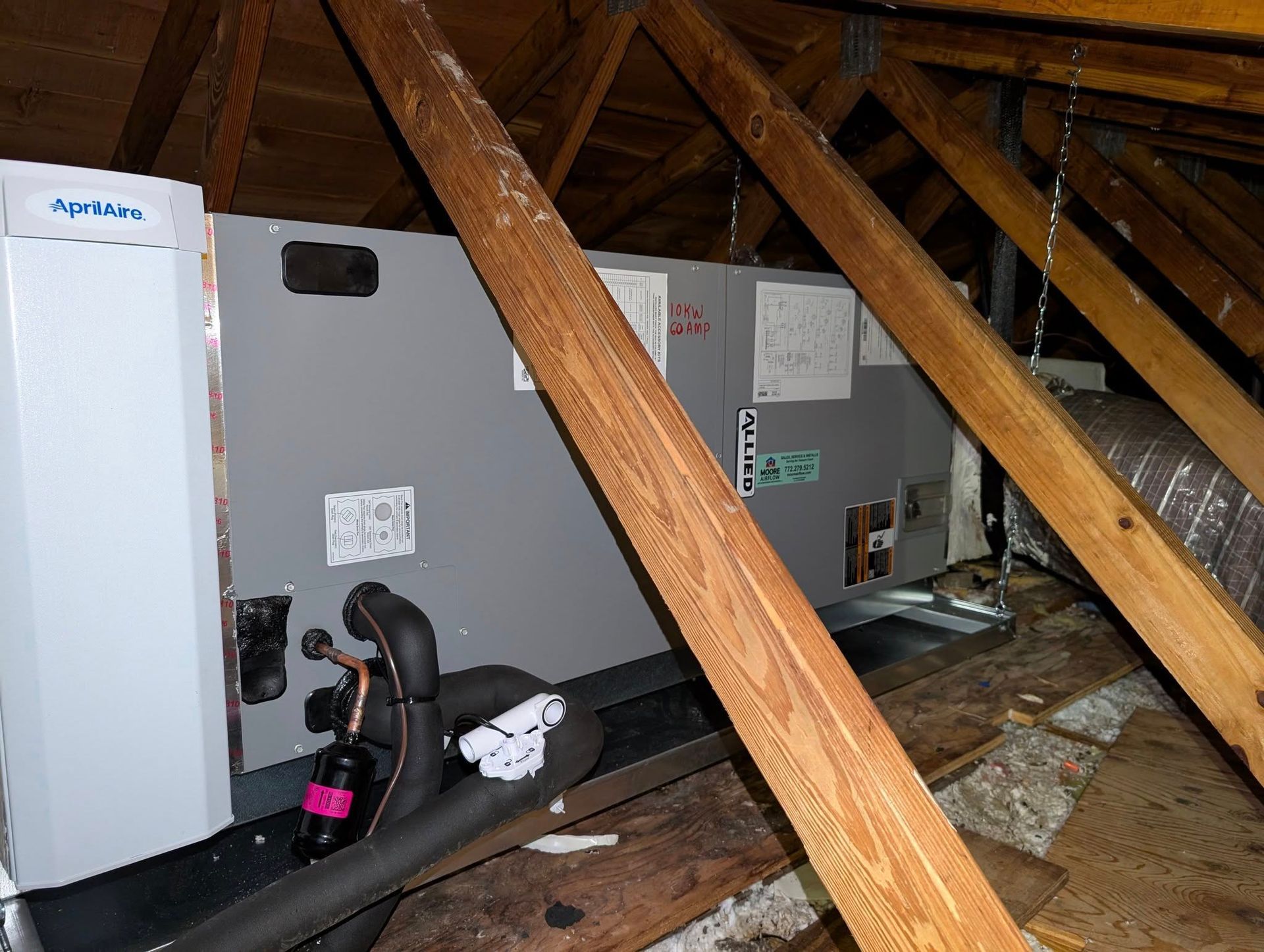 An air conditioner is sitting in the attic between two wooden beams.