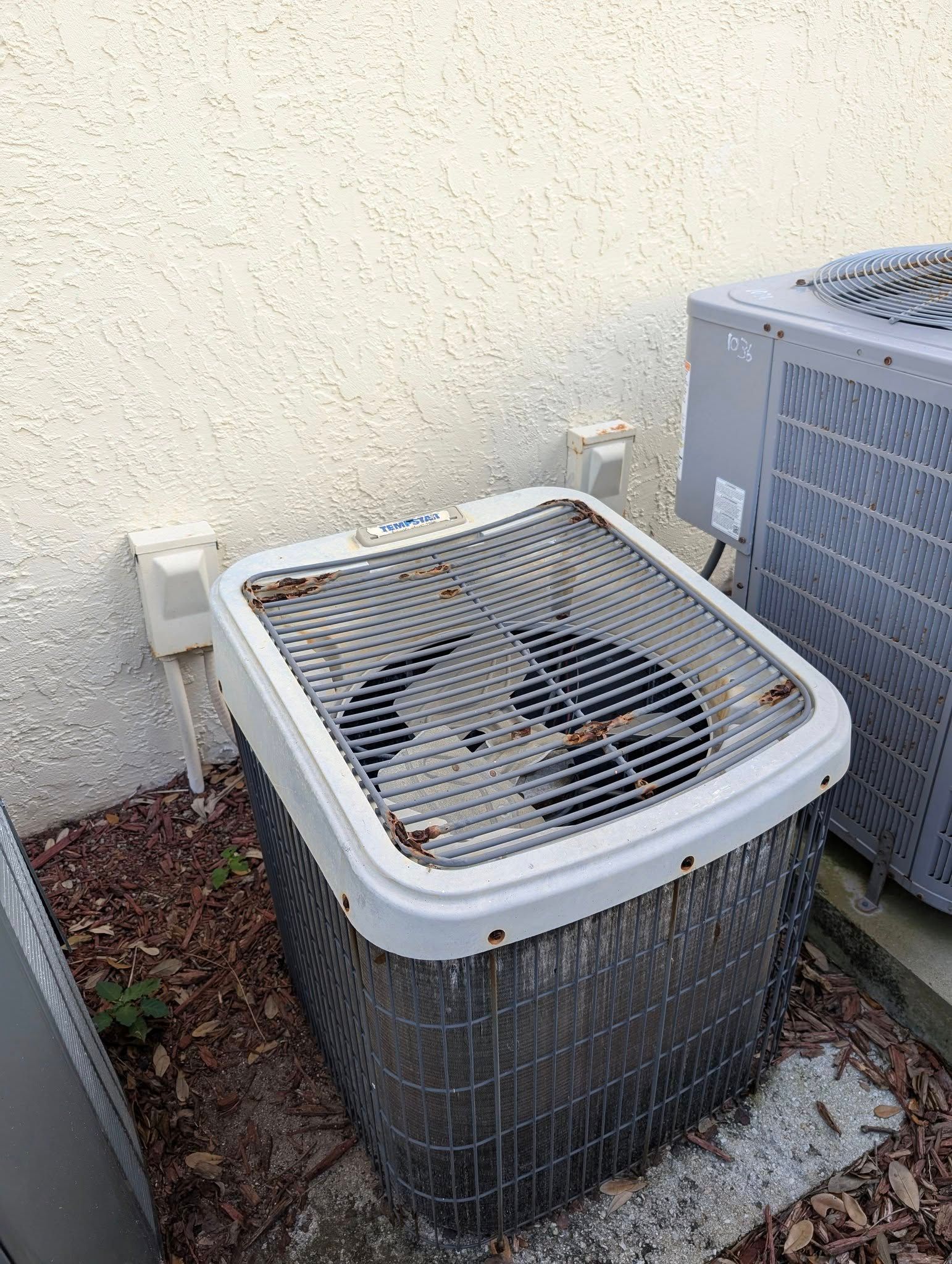 A dirty air conditioner is sitting next to a wall.