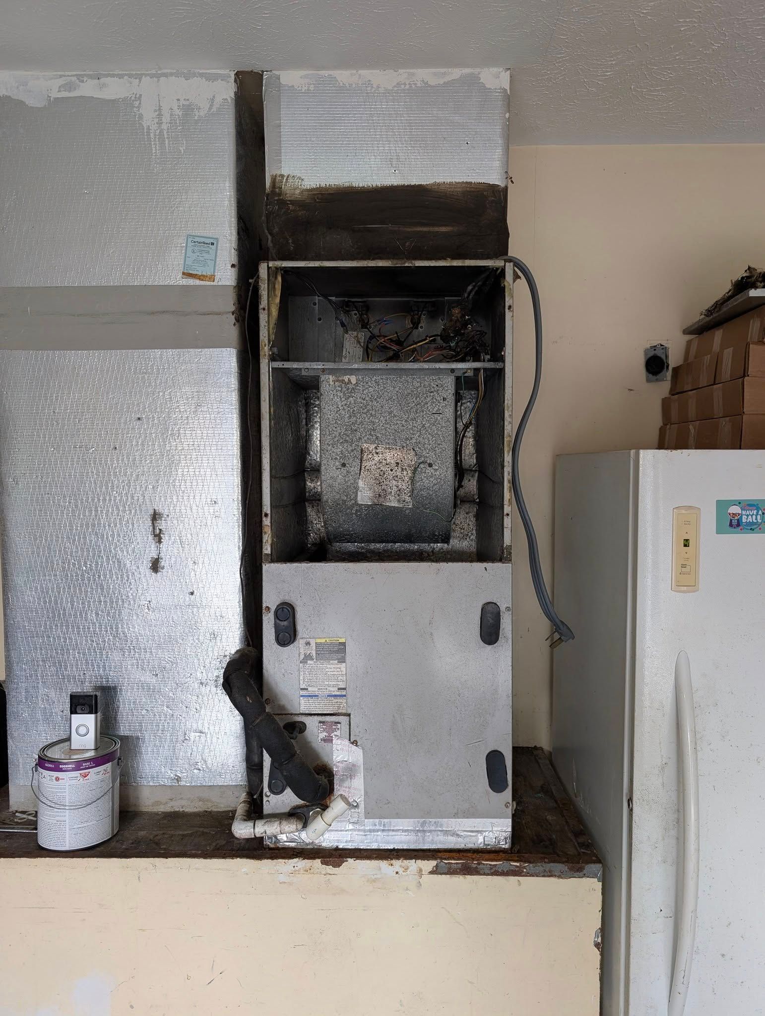 A broken air conditioner is sitting in a kitchen next to a refrigerator.